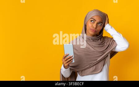 Donna musulmana pensierosa che tiene uno smartphone e si tocca la testa Foto Stock
