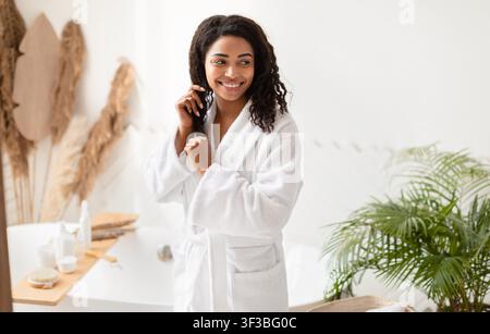 Donna Africana americana che tocca i capelli dopo la doccia in posa in bagno Foto Stock