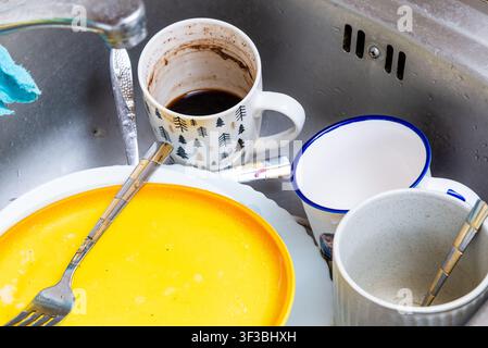 Piatti sporchi in un lavello da cucina in acciaio inossidabile. Lavello da cucina disordinato pieno di tazze, piatti e posate non lavati. Foto Stock
