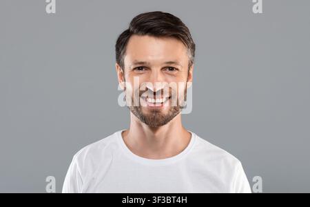 Bell'uomo caucasico che sorride alla macchina fotografica su grigio Foto Stock