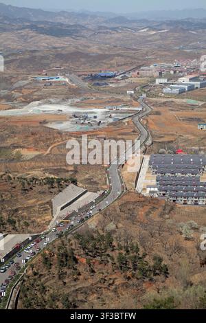 Fotografia aerea ad angolo alto che cattura una strada asfaltata sinuosa che attraversa un paesaggio rurale semi-arido. La scena presenta colline brune sterili, spar Foto Stock