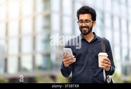 Allegro indiano che va in ufficio, usa il telefono, beve caffè Foto Stock
