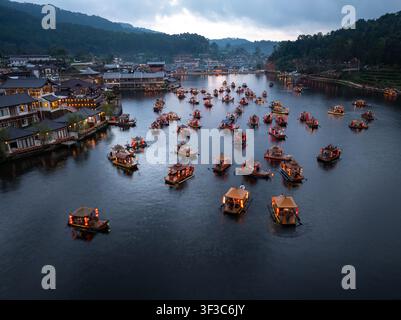 Barche di legno illuminate tradizionali galleggiano su un lago calmo al crepuscolo a Ban Rak Thai Mae Hong Son Thailandia. Foto Stock