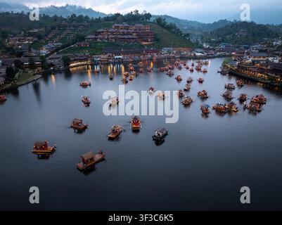 Raft di legno illuminati galleggiano su un lago calmo al crepuscolo nel villaggio di Ban Rak Thai, Mae Hong Son, Thailandia Foto Stock