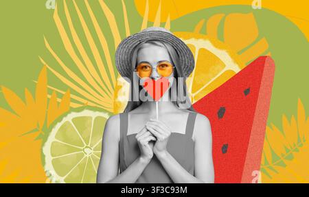 Giovane donna sorridente che tiene un lecca-lecca a forma di cuore su uno sfondo colorato, concetto estivo Foto Stock
