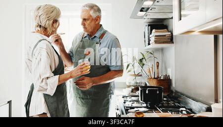Cucina, gusto e coppia di anziani in cucina per la preparazione, il legame e l'aiuto per la cena a casa. Matrimonio, felice e uomo con donna con cucchiaio, bevanda Foto Stock