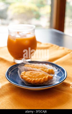 Puff di curry thailandese tradizionali serviti con tè al latte thailandese freddo in un accogliente caffè Foto Stock