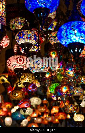 Colpo ravvicinato verticale di lampade in vetro a mosaico turche vibranti e luminose e lanterne orientali appese in un negozio. Concetto ideale per l’artigianato tradizionale, la cultura orientale, il souvenir del Grande Bazar, il design dell’illuminazione interna, l’arredamento del Medio Oriente e le mete turistiche. Foto Stock