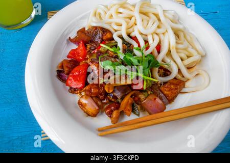 Kung Pao piccante con noodle udon, bacchette su piatto bianco su tavolo blu, primo piano. Foto Stock