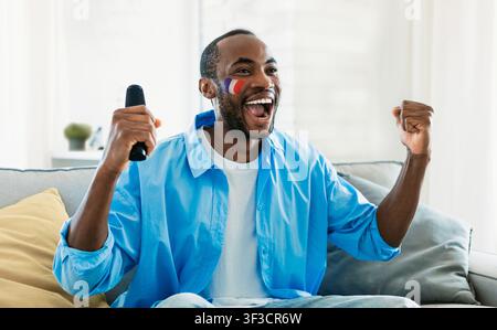 Uomo afroamericano eccitato che celebra guardando lo sport a casa, emozione felice Foto Stock