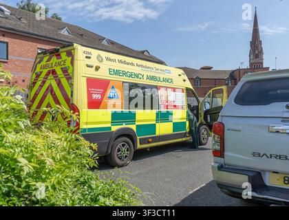 Vista laterale di un'ambulanza di emergenza britannica parcheggiata con un membro dell'equipaggio appoggiato nella cabina anteriore. Foto Stock