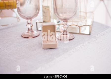 Anello di fidanzamento con diamante in una scatola di velluto su un tavolo romantico apparecchiato con bicchieri di vino rosa, champagne e frutta, una proposta di matrimonio e una celebrazione Foto Stock
