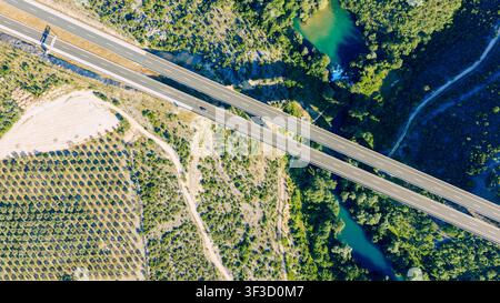 Vista aerea dall'alto di un moderno ponte autostradale che attraversa un fiume smeraldo attraverso una valle verde Foto Stock