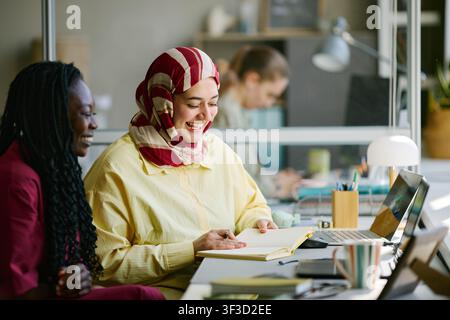Donna nera e donna musulmana collaborano in un ufficio moderno Foto Stock