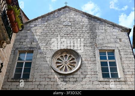 Prima pianura di una facciata di chiesa in pietra medievale con una finestra a rosa intagliata in modo intricato, motivo a croce e muratura antica, rappresentativa dell'architettura sacra europea tradizionale Foto Stock