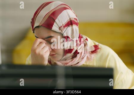 Donna musulmana adulta che sperimenta affaticamento oculare durante il lavoro Foto Stock