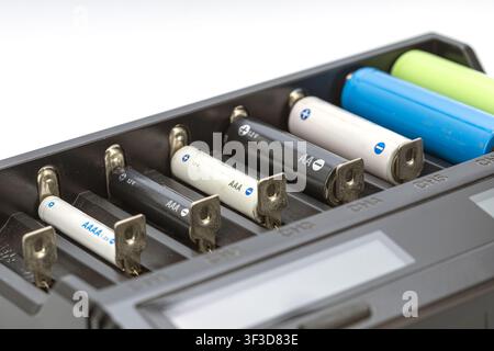 Caricatore intelligente universale con più dimensioni di batterie ricaricabili AA, AAA, AAAA e celle al litio 18650 in slot individuali su sfondo bianco Foto Stock