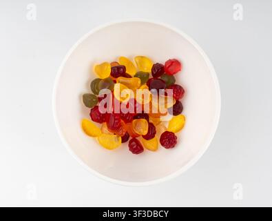 Caramelle gommose di frutta in una ciotola isolata, pillole vegane di marmellata da masticare, cumulo di gocce di gelatina, caramelle colorate su sfondo bianco dall'alto Foto Stock