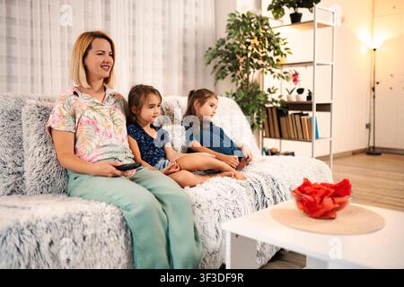 Madre e figlie che guardano la televisione insieme in salotto Foto Stock