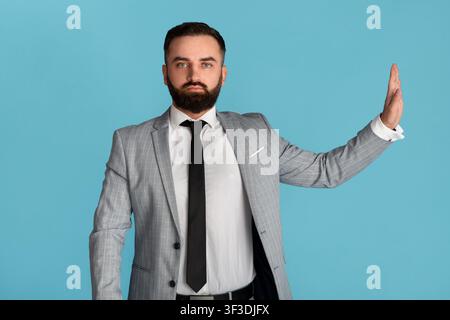 Dipendente serio che mostra il gesto di stop, esprimendo il rifiuto su sfondo blu Foto Stock