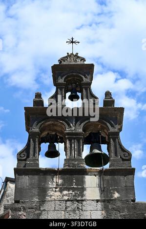 Vista ad angolo basso di un vecchio campanile in pietra con campane di bronzo e una croce di metallo in cima, sullo sfondo un cielo blu nuvoloso. Ideale per concetti di religione, spiritualità, storia, eredità cristiana e architettura europea. Foto Stock