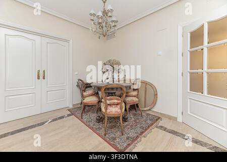 Angolo pranzo classico con un tavolo rotondo in legno, sedie imbottite vintage, un lampadario e un grande specchio ovale. Foto Stock