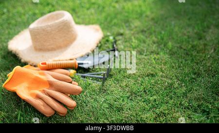 Guanti da giardinaggio, cappello di paglia e attrezzi manuali disposti su erba verde fresca. Attrezzature da giardino per la semina primaverile e lavori all'aperto in cortile. Copia Foto Stock