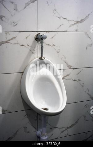 Urinale in ceramica bianca montato su una parete di bagno piastrellata in marmo Foto Stock