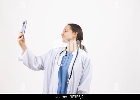 Medica che scatta un selfie su smartphone con camice da medico Foto Stock