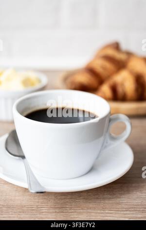 Caffè nero con croissant freschi su tavolo di legno Foto Stock