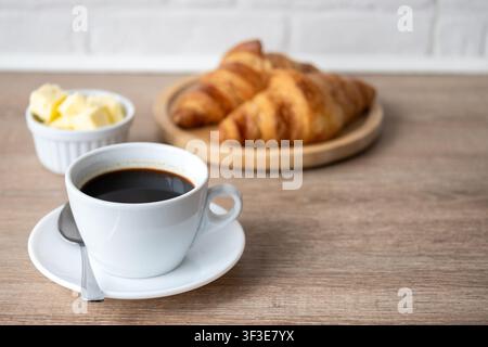 Caffè nero con croissant freschi su tavolo di legno Foto Stock