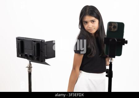 Blogger femmina che registra contenuti video su uno smartphone montato su treppiede Foto Stock