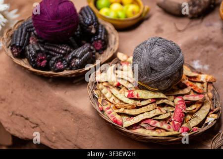Vista ad angolo alto degli ingredienti tradizionali per tinture naturali peruviane, che mostra una palla di filo viola su mais viola e una palla di filo grigia su baccelli di tara essiccati Foto Stock