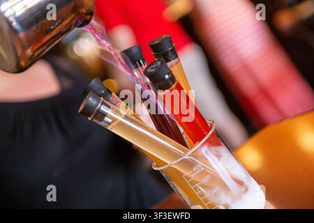 Un barista versa un liquido infiammabile su un volo novelty di shot di cocktail in provetta per creare una breve fiamma. Foto Stock