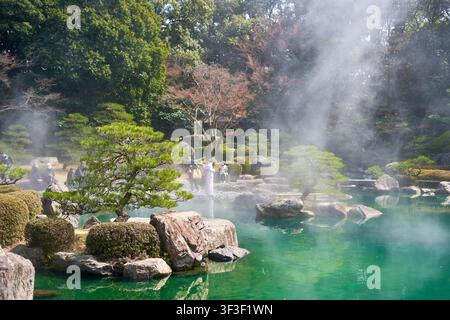 Una scena serena di giardino giapponese con uno stagno verde smeraldo circondato da pini accuratamente potati, grandi rocce e vegetazione lussureggiante. Nebbia Foto Stock