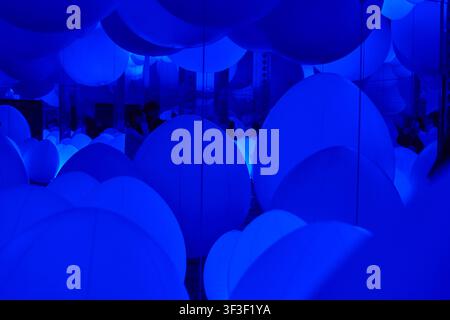 Un'installazione artistica immersiva con numerosi grandi oggetti sferici blu luminosi sospesi in una stanza buia. Le sfere variano in dimensione e Foto Stock
