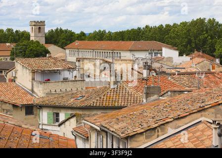 Vista dal tetto sulle tegole in terracotta dei vecchi case in pietra di Arles, Francia, con il campanile della chiesa sullo sfondo. Foto Stock