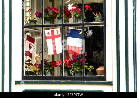 In una finestra su Old Post Road a Grand Pré, nella Nuova Scozia, Canada, la bandiera canadese, la bandiera del Grande Consiglio dei Mi’kmaq (Santé Mawiómi) e la bandiera acadiana sono appese fianco a fianco tra vasi di geranioli. Questa combinazione rappresenta i Mi’kmaq come popolo indigeno, i coloni acadiani e il Canada moderno, che hanno tutti plasmato la storia della regione Foto Stock