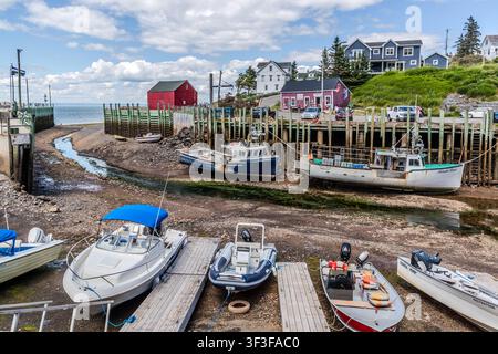 Con la bassa marea, diverse barche sono ormeggiate al molo su West Halls Harbour Road a Halls Harbour, nella Nuova Scozia, Canada. Case residenziali si trovano sul pendio che si affaccia sulla baia; la città è stata chiamata in onore del corsaro americano Samuel Hall, che fuggì qui dai soldati della milizia nel 1779 Foto Stock