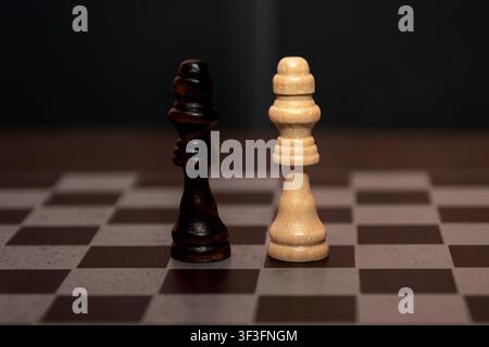 Re bianco e re nero in piedi faccia a faccia su una scacchiera, un confronto minimalista che simboleggia il duello tra il bene e il male, l'equilibrio e ri Foto Stock
