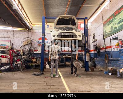 Tecnici automobilistici che eseguono un'ispezione del veicolo su un ponte idraulico in un'officina di riparazione, la foto è stata scattata a Jodhpur, Rajasthan, India, il 10 luglio 2026. Foto Stock