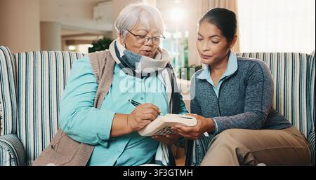 Badante, anziana e scrittura a casa con libro, ricerca di parole e cruciverba per l'assistenza sanitaria. Infermiera, aiuto e persona anziana a casa con sudoku Foto Stock