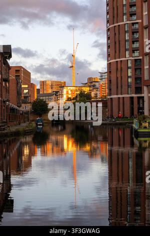 Appartamenti sul lungomare di Leeds e canale che riflette luce dorata accanto a una gru per costruzioni Foto Stock