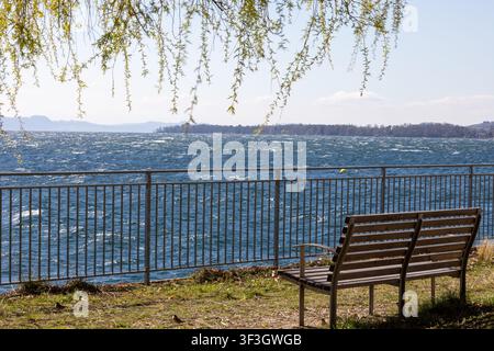 Panchina di legno vuota che si affaccia sul Lago di Neuchâtel in una giornata di primavera soleggiata nell'occidente della Svizzera. Foto Stock