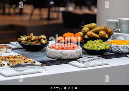 Un buffet di frutta fresca con pompelmo, kiwi, uva, pere e arance, esposto a un moderno banco colazione di hotel. Foto Stock