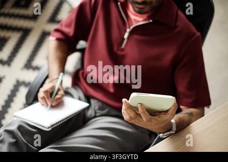 Uomo adulto che usa una calcolatrice e prende appunti mentre lavora Foto Stock