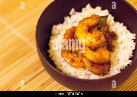 Vista dall'alto di gamberetti cotti in pasta di curry rosso serviti su riso jasmine al vapore in una ciotola scura, una ricetta saporita di ispirazione asiatica Foto Stock