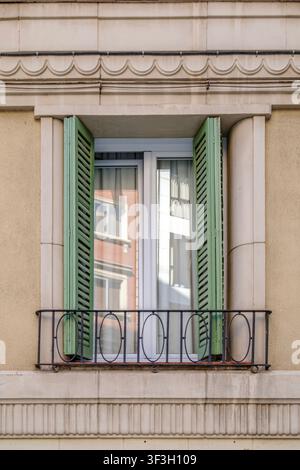 Barcellona – Spagna – 14 luglio 2026: Finestra classica con persiane verdi aperte, balcone in ferro, facciata ornata, riflessione Foto Stock