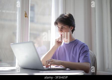 Giovane uomo pensieroso che lavora su un computer portatile Foto Stock