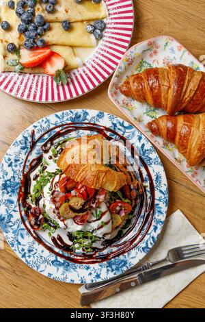 Prima piano di un croissant farcito con burrata mozzarella, pomodori e capperi, condito con salsa, su uno sfondo solido. Foto Stock